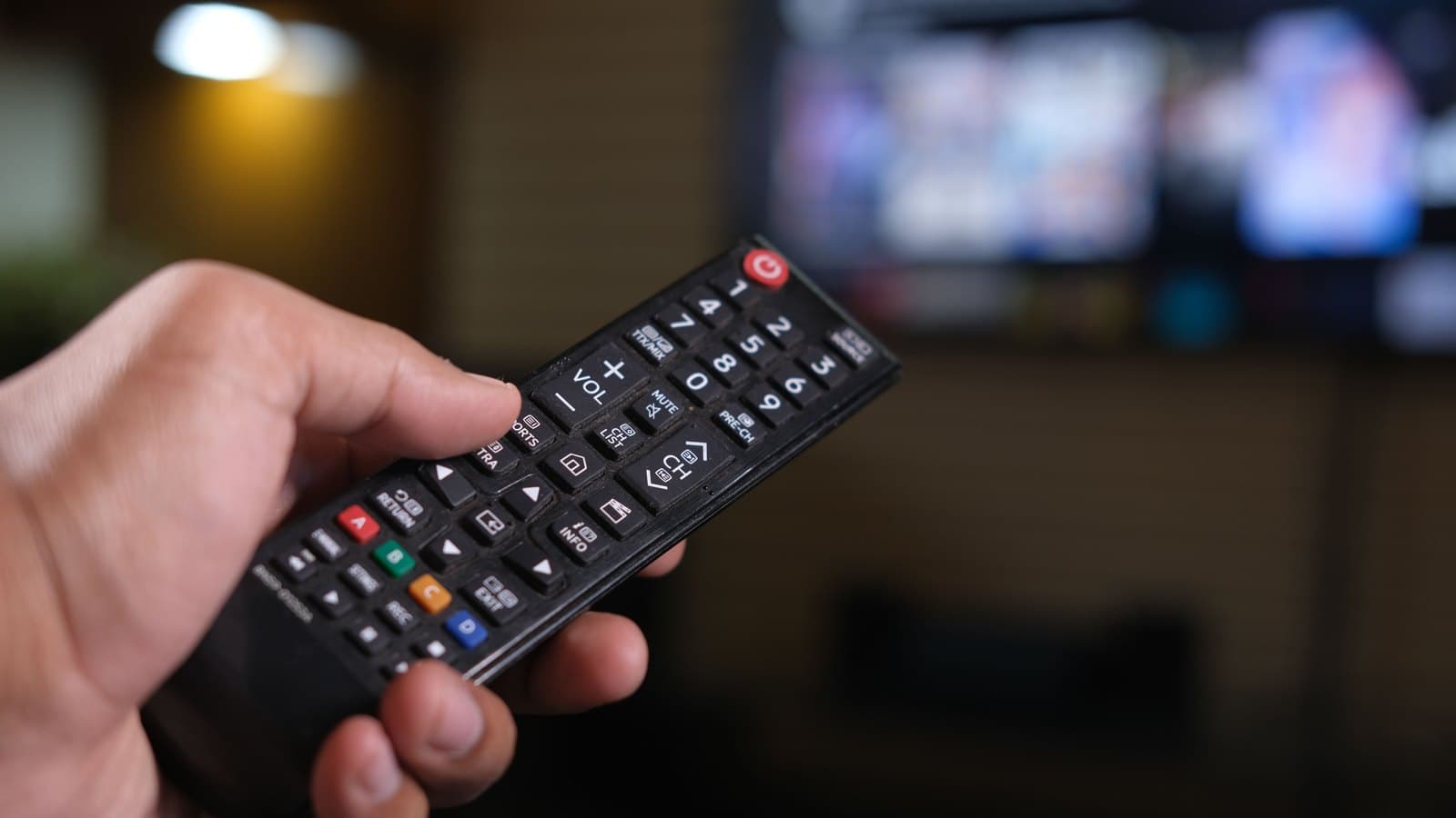 Dłoń z pilotem telewizora skierowanym w stronę ekranu z listą aplikacji — aktywacja dostępu IPTV kodem