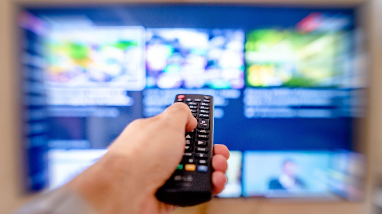 Dłoń z pilotem skierowanym w stronę telewizora z aplikacją do oglądania telewizji internetowej OTT Navigator